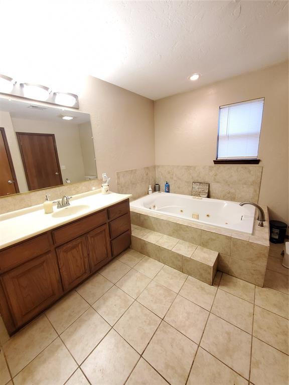 bathroom with tile patterned flooring, tiled tub, vanity, and a textured ceiling