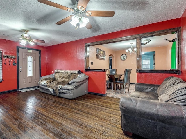 living room with dark wood-type flooring, ceiling fan with notable chandelier, and a textured ceiling