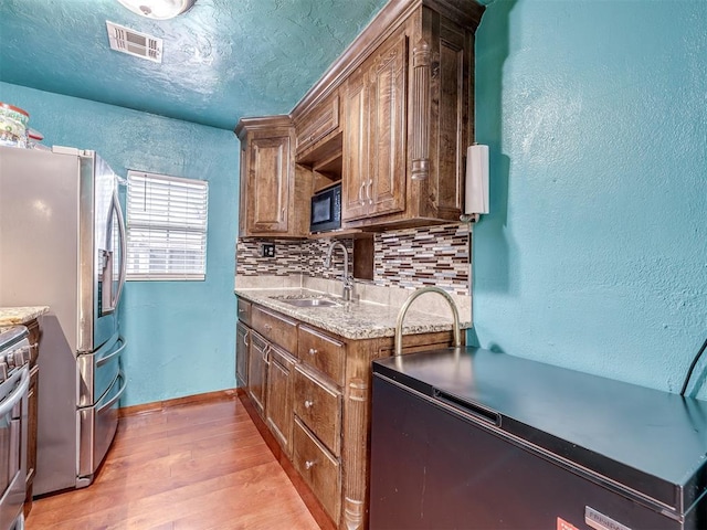 kitchen featuring appliances with stainless steel finishes, sink, decorative backsplash, light hardwood / wood-style floors, and a textured ceiling