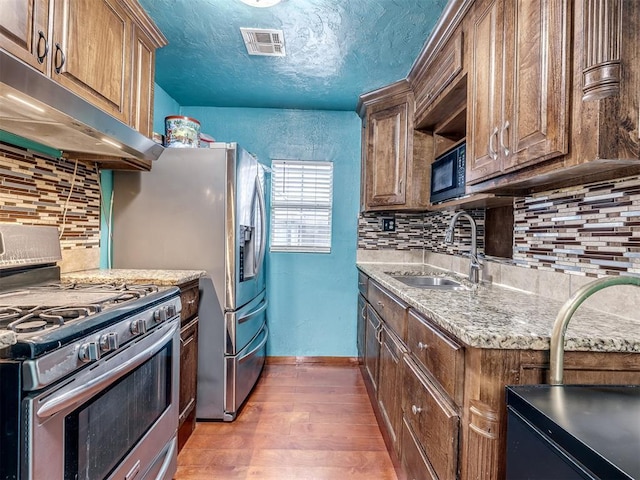 kitchen with dark wood-type flooring, sink, a textured ceiling, stainless steel range with gas stovetop, and light stone countertops