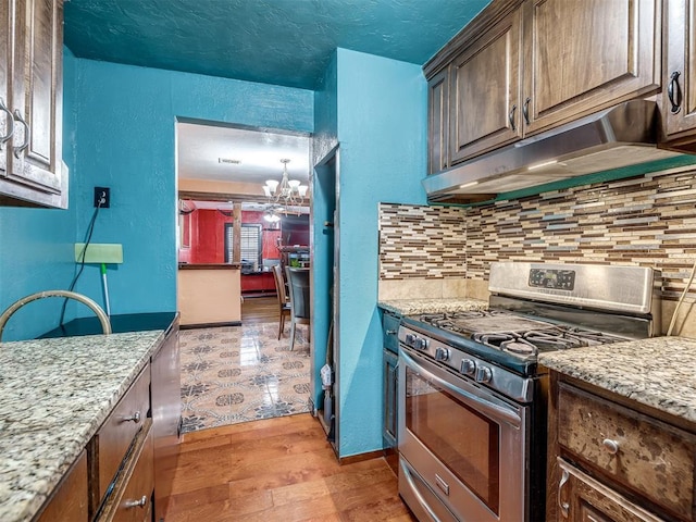 kitchen featuring tasteful backsplash, a chandelier, light wood-type flooring, stainless steel range with gas stovetop, and light stone countertops