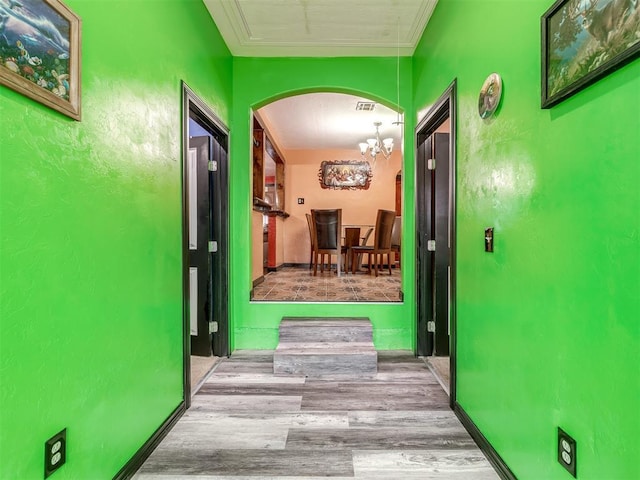 hall featuring crown molding, light hardwood / wood-style floors, and a notable chandelier