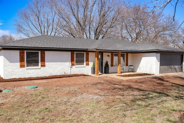 single story home with an attached garage, a shingled roof, and brick siding