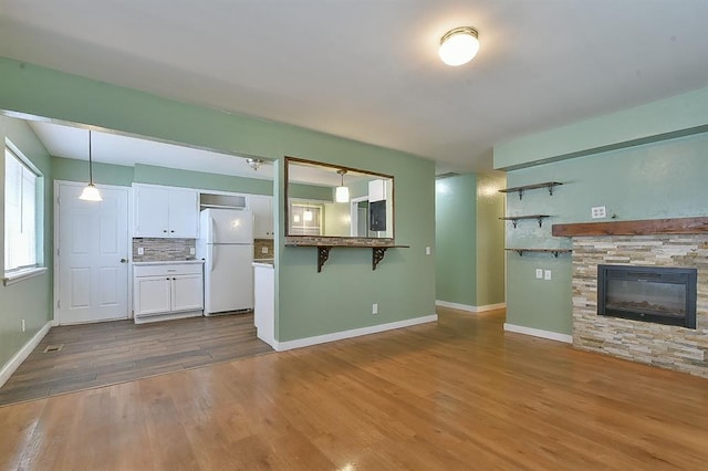 kitchen with a stone fireplace, pendant lighting, white cabinetry, decorative backsplash, and white refrigerator