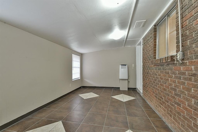 unfurnished room featuring brick wall and dark tile patterned floors