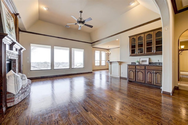 living room with a brick fireplace, ceiling fan with notable chandelier, dark wood-type flooring, and vaulted ceiling