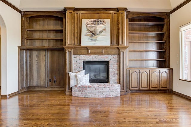 unfurnished living room with wood-type flooring, crown molding, a fireplace, and built in shelves