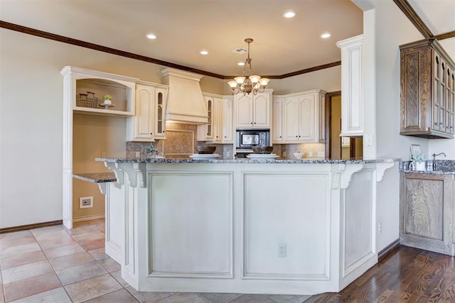 kitchen with stainless steel microwave, kitchen peninsula, custom range hood, and dark stone countertops