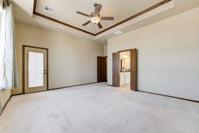 unfurnished bedroom with connected bathroom, light colored carpet, ceiling fan, a tray ceiling, and crown molding