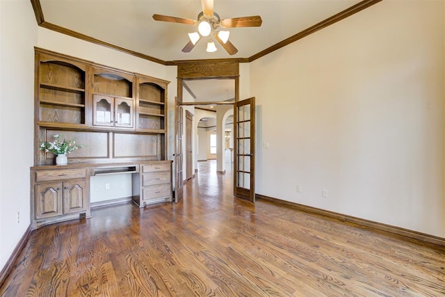 unfurnished office with french doors, dark wood-type flooring, crown molding, built in desk, and ceiling fan