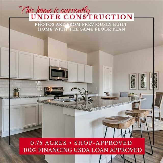 kitchen featuring appliances with stainless steel finishes, an island with sink, dark stone counters, dark hardwood / wood-style flooring, and white cabinetry