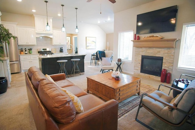 living room with lofted ceiling, a healthy amount of sunlight, a stone fireplace, and sink