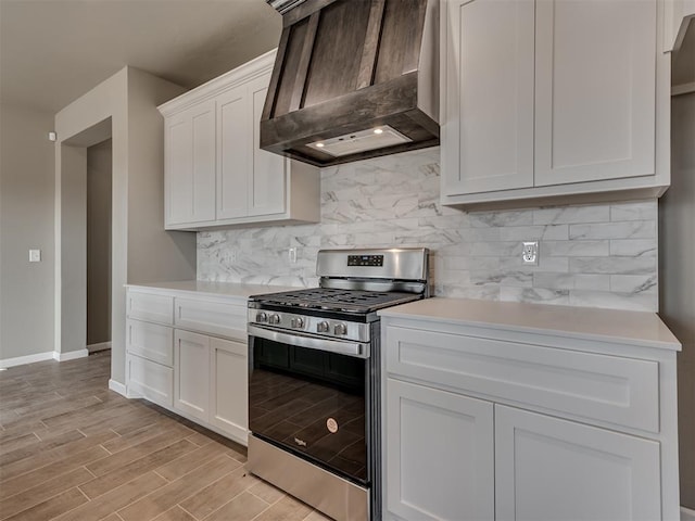 kitchen featuring stainless steel range with gas cooktop, white cabinetry, backsplash, custom range hood, and light hardwood / wood-style flooring