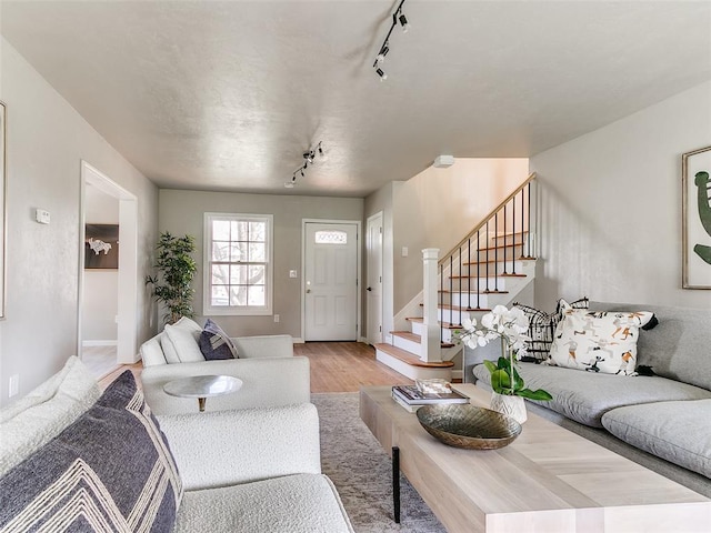 living area with track lighting, baseboards, stairs, and light wood-style flooring