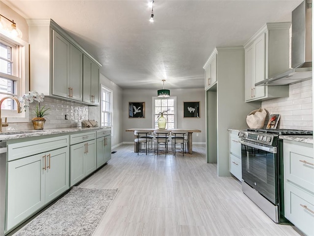 kitchen with baseboards, wall chimney range hood, a sink, backsplash, and gas stove