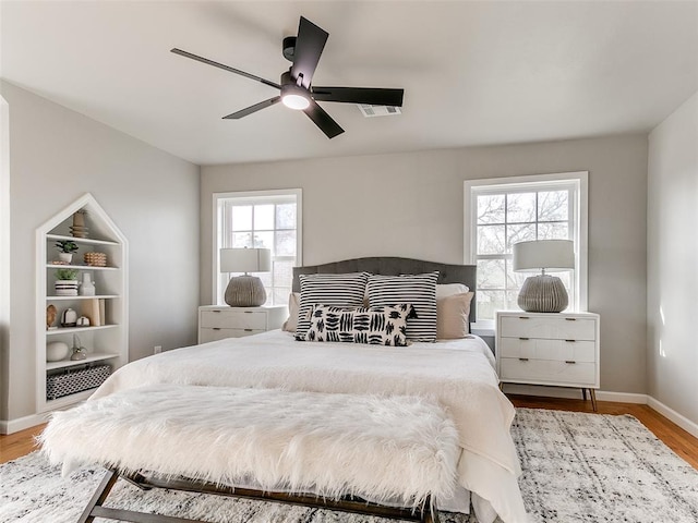 bedroom with baseboards, ceiling fan, wood finished floors, and visible vents