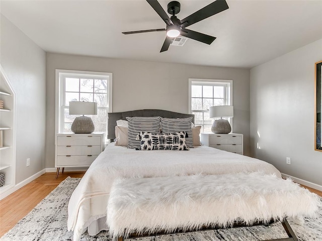 bedroom featuring baseboards, a ceiling fan, wood finished floors, and visible vents