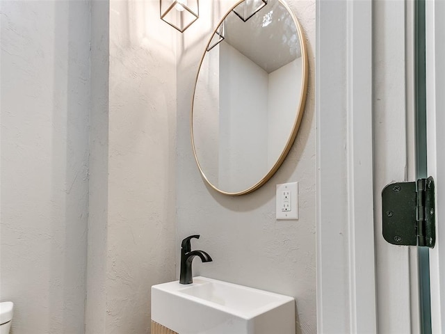 bathroom featuring toilet, a textured wall, and a sink