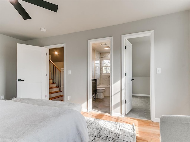 bedroom featuring a walk in closet, ensuite bathroom, baseboards, and light wood finished floors