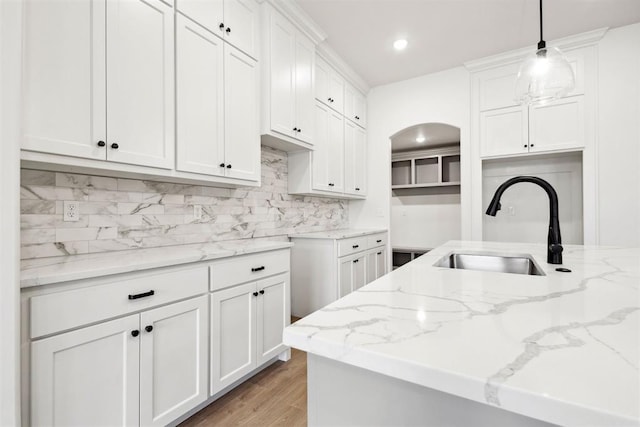 kitchen featuring sink, white cabinets, light stone counters, and decorative light fixtures