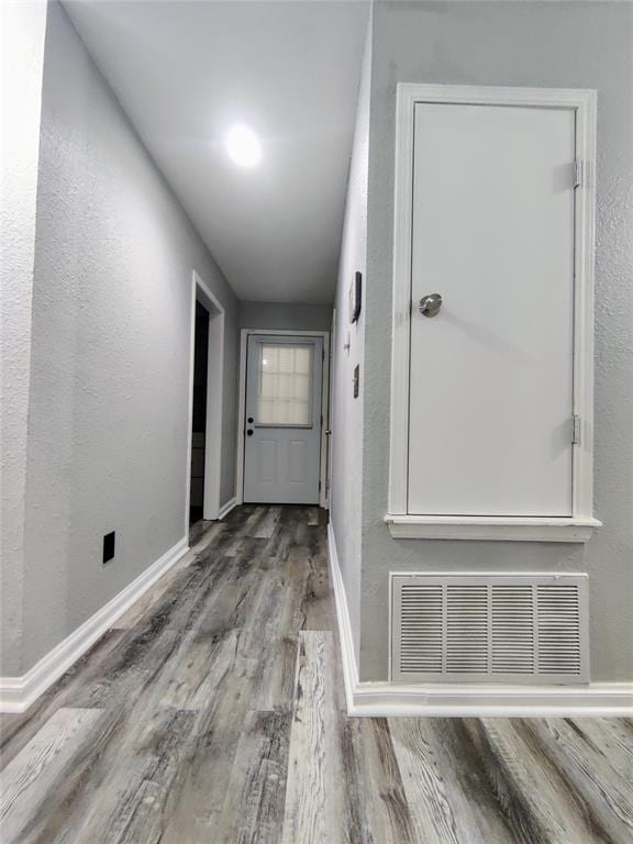 hall with baseboards, visible vents, a textured wall, and wood finished floors