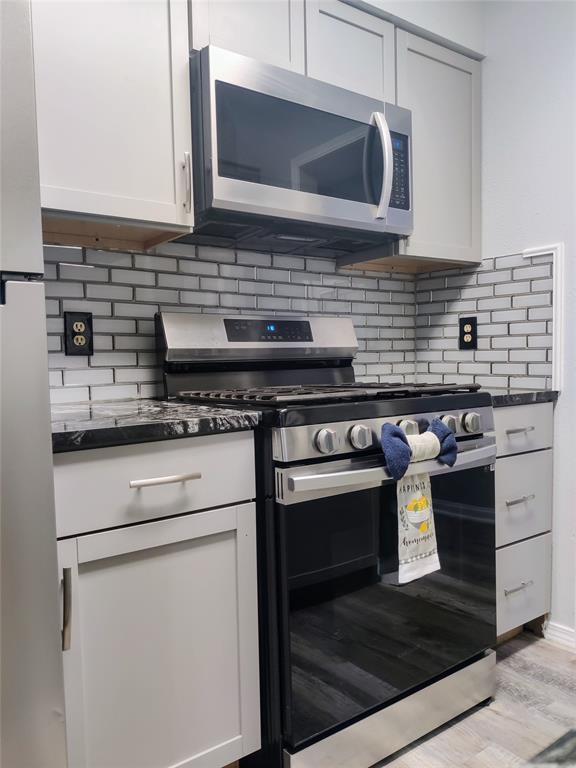 kitchen with light wood-style flooring, dark countertops, white cabinetry, backsplash, and appliances with stainless steel finishes