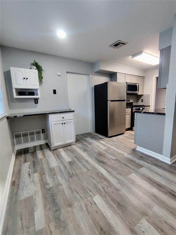 kitchen featuring stainless steel appliances, visible vents, light wood finished floors, white cabinets, and dark countertops