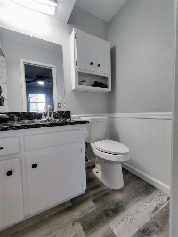 half bathroom with vanity, toilet, wood finished floors, and wainscoting