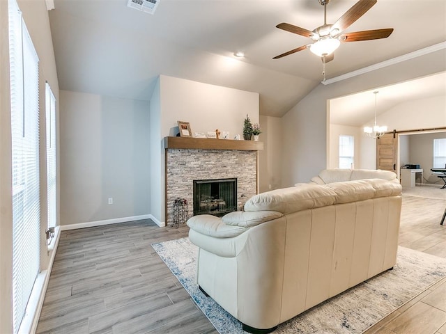 living room with a fireplace, vaulted ceiling, ceiling fan, a barn door, and light hardwood / wood-style floors