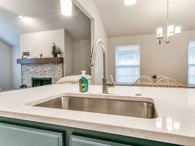 kitchen with a stone fireplace, decorative light fixtures, sink, a chandelier, and light stone counters