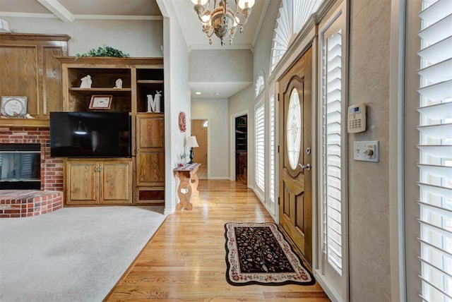 foyer with an inviting chandelier, crown molding, a fireplace, and light wood-type flooring