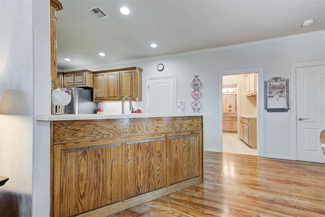 kitchen with sink, stainless steel fridge, ornamental molding, light hardwood / wood-style floors, and kitchen peninsula