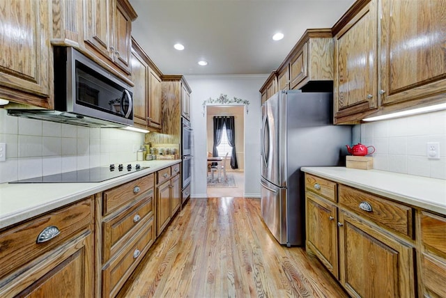 kitchen featuring stainless steel appliances, ornamental molding, tasteful backsplash, and light hardwood / wood-style flooring