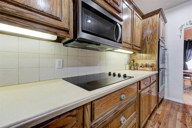 kitchen with backsplash, light hardwood / wood-style flooring, ornamental molding, and appliances with stainless steel finishes