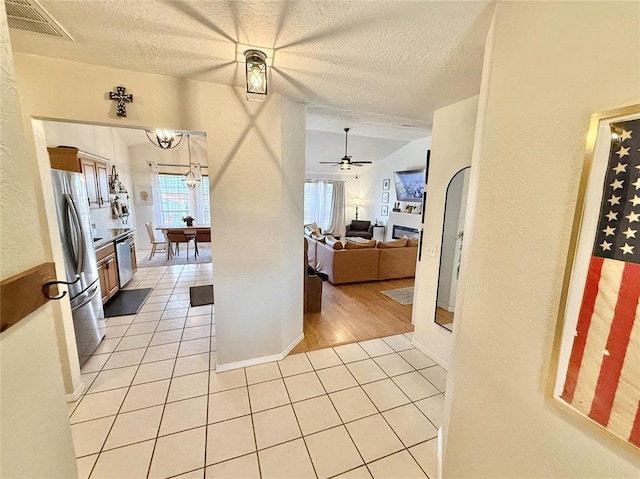 kitchen with ceiling fan with notable chandelier, appliances with stainless steel finishes, light tile patterned floors, and a textured ceiling