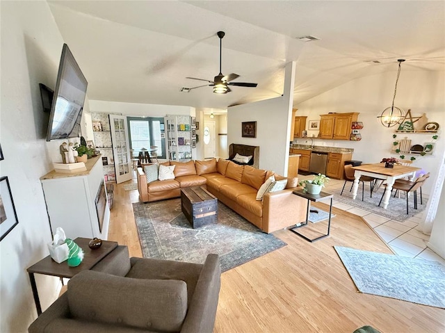 living room featuring ceiling fan with notable chandelier, vaulted ceiling, and light wood-type flooring