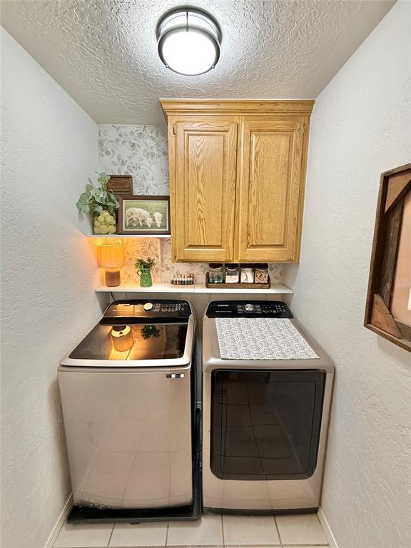 washroom with cabinets, washer and clothes dryer, a textured ceiling, and light tile patterned floors