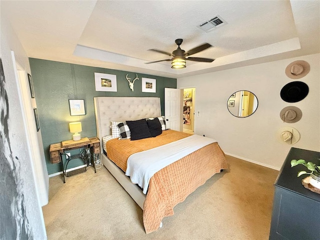 carpeted bedroom with a raised ceiling and ceiling fan