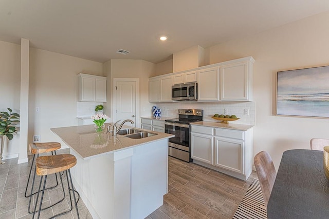 kitchen with stainless steel appliances, a sink, white cabinets, wood tiled floor, and a center island with sink