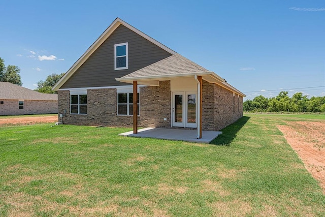 back of property with a lawn, a patio, roof with shingles, french doors, and brick siding