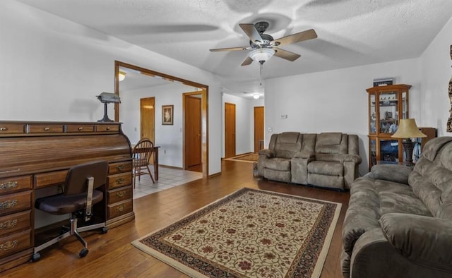 living room featuring ceiling fan, a textured ceiling, and light wood-type flooring