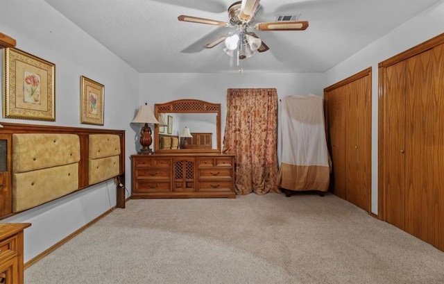 bedroom with light carpet, two closets, and ceiling fan