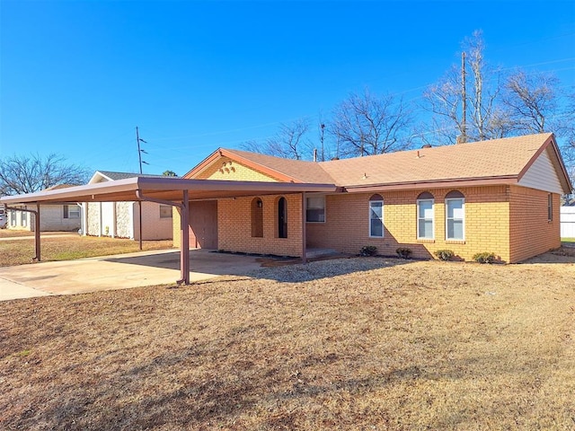 rear view of property featuring a carport, a yard, brick siding, and driveway