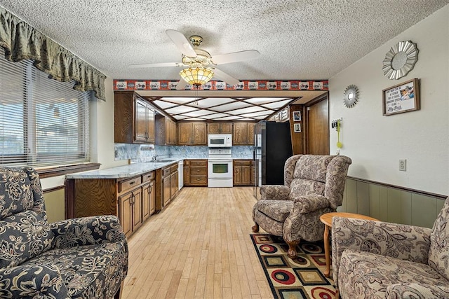 kitchen featuring sink, a textured ceiling, light wood-type flooring, white appliances, and backsplash