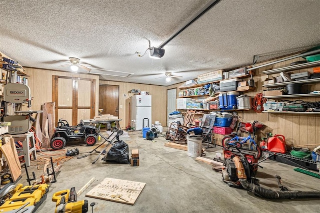 garage with a garage door opener, white fridge, wooden walls, and ceiling fan