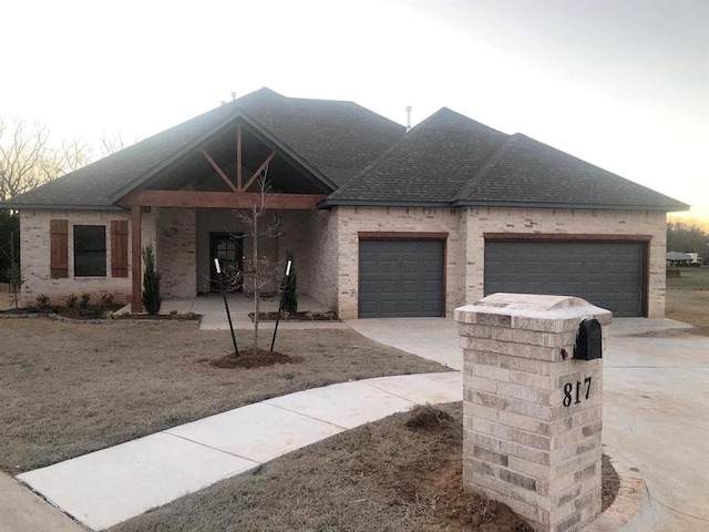 view of front of house with a garage, concrete driveway, roof with shingles, and brick siding