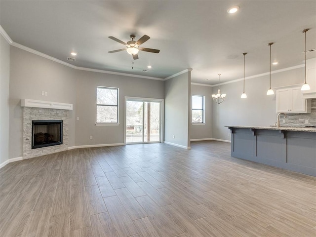 817 Carrie Ct, Purcell, OK 73080 - unfurnished living room with baseboards, ceiling fan with notable chandelier, a stone fireplace, and light wood finished floors