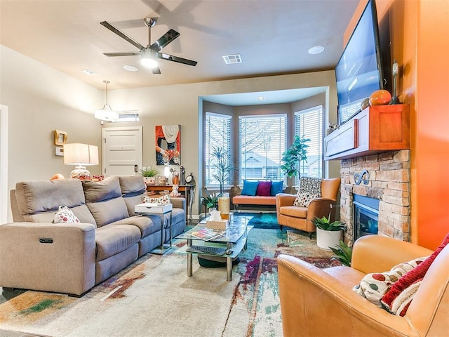 carpeted living room with a stone fireplace and ceiling fan