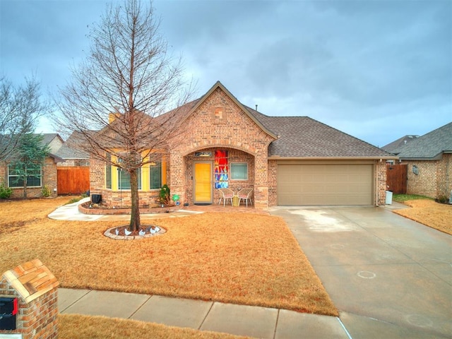 view of front of property with fence, concrete driveway, an attached garage, a shingled roof, and brick siding