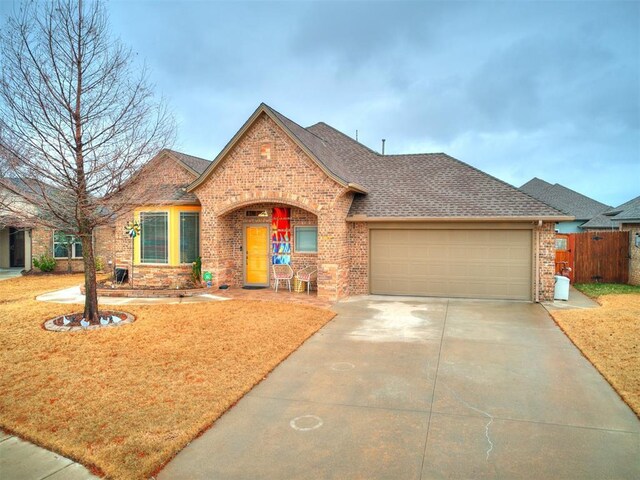 view of front of property featuring fence, driveway, roof with shingles, an attached garage, and brick siding